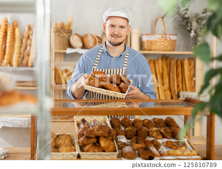Selling fresh croissants in bakery - Baker places hot croissants on display Selling fresh croissants in bakery - Baker places hot croissants on display 125810789