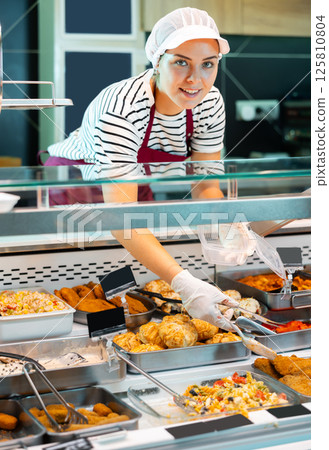 Friendly salesgirl filling container with ready-to-eat food in supermarket Friendly salesgirl filling container with ready-to-eat food in supermarket 125810804