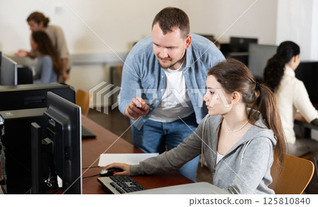 During computer lesson, male teacher helps girl student complete difficult task 125810840