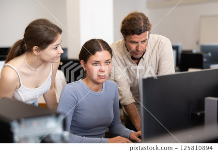During computer lesson, two companions help girl student complete difficult task 125810894