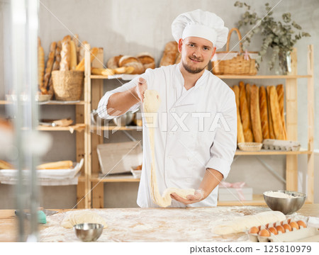 Process of making baguette, loaf or bread in bakery - baker kneads and rolls the dough to give the shape of future bread 125810979