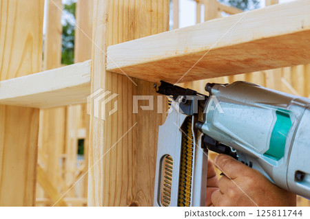 Skilled laborer operates air nail gun to secure wooden beams in construction site during works day 125811744