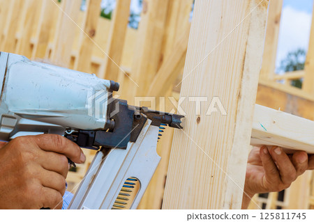 Craftsman during teamwork nail gun to fasten wooden beam at construction site 125811745