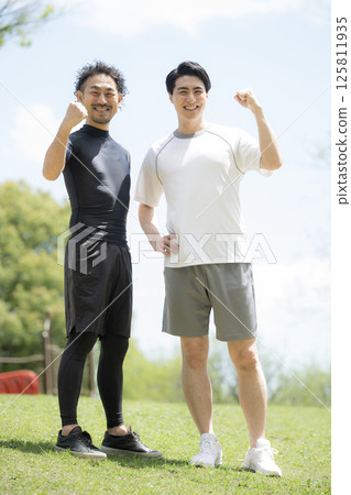 Two refreshing men playing sports together under the blue sky, looking at the camera and making a fist pump Two refreshing men playing sports together under the blue sky, looking at the camera and making a fist pump 125811935