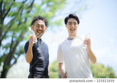 Two refreshing men playing sports together under the blue sky, looking at the camera. Image of hydration in summer with plastic bottles 125811939