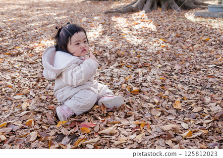 [One-year-old child sitting and playing in a winter park covered with fallen leaves] 125812023