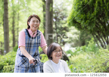 微笑的護理人員和老年人在綠地中漫步，看著鏡頭日間護理服務和日間護理上門護理的形象 125812050