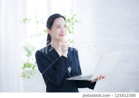 A woman looking up and thinking positively while holding a laptop A woman looking up and thinking positively while holding a laptop 125812380