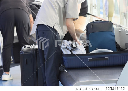 Foreign tourists packing their suitcases in the airport departure lobby Foreign tourists packing their suitcases in the airport departure lobby 125813412