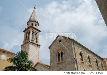 Budva, Montenegro picturesque old town and fortress walls architecture. Stunning showcasing historic stone buildings with red-tiled roofs traditional house. Spire of the chapel of The Church of Sveti 125813506