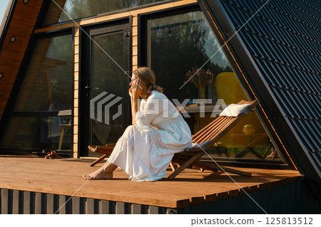 Pensive woman sitting on chair on terrace of log house 125813512