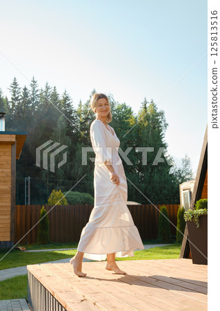 Cheerful woman waiving her dress standing on warm wooden terrace 125813516
