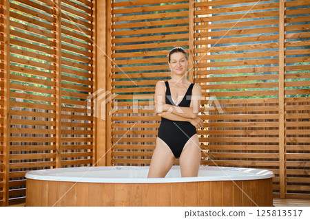 Glad woman stands with folded arms in a hot tub outdoors 125813517