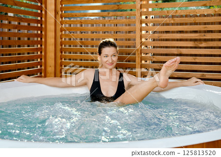 Playful woman stretching her foot in hot tub Playful woman stretching her foot in hot tub 125813520