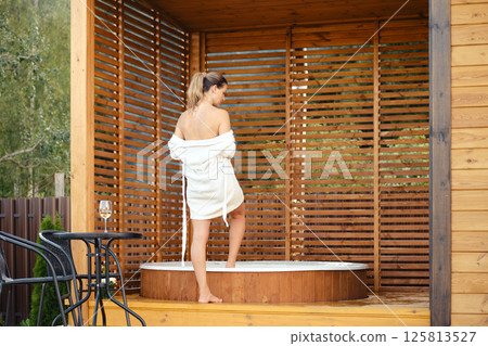 View of a woman removing her robe and entering the outdoor jacuzzi View of a woman removing her robe and entering the outdoor jacuzzi 125813527