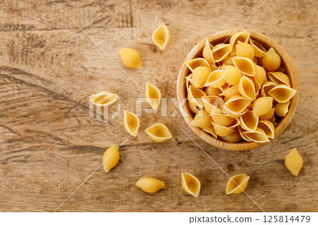 Raw uncooked dried Conchiglie shell pasta. Italian seashells pasta in wooden bowl on wooden background. 125814479