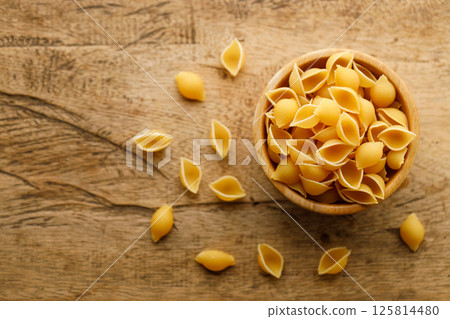 Raw uncooked dried Conchiglie shell pasta. Italian seashells pasta in wooden bowl on wooden background. 125814480