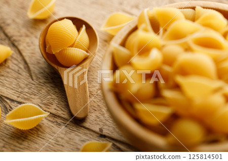 Raw uncooked dried Conchiglie shell pasta. Italian seashells pasta in wooden bowl on wooden background. 125814501
