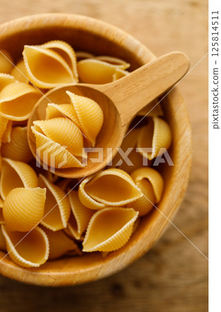 Raw uncooked dried Conchiglie shell pasta. Italian seashells pasta in wooden bowl on wooden background. Raw uncooked dried Conchiglie shell pasta. Italian seashells pasta in wooden bowl on wooden background. 125814511