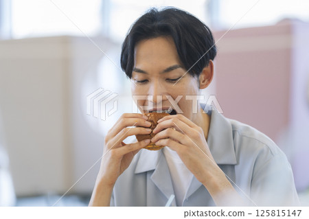 A man in his 30s eating a hamburger 125815147