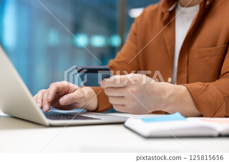 Asian businessman using credit card and laptop for online payment. Image captures essence of modern finance, technology, e-commerce, and business transactions with focus on convenience. Asian businessman using credit card and laptop for online payment. Image captures essence of modern finance, technology, e-commerce, and business transactions with focus on convenience. 125815656