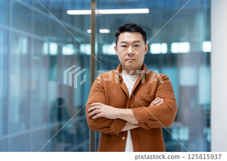 Serious mature man with crossed arms inside office at workplace looking at camera. Successful asian businessman investor, in casual clothes standing near window. 125815937