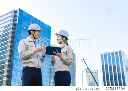 A group of male and female engineers having a meeting while looking at a tablet at a construction site 125817304