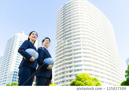 一群商人戴著頭盔站在綠樹成蔭的城市前 125817309