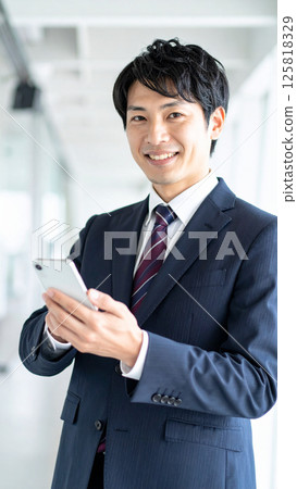 Smiling young businessman holding a smartphone (AI generated image) 125818329