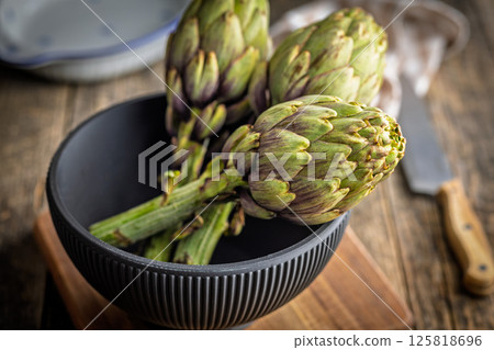 Ripe artichokes plant in bowl on wooden table. 125818696
