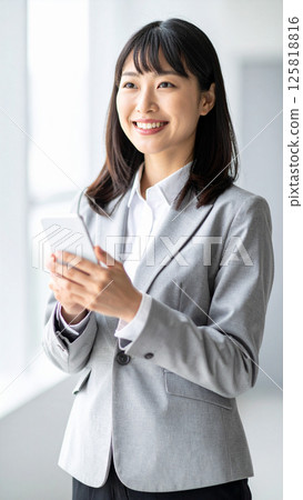 微笑的年輕女商人拿著智慧型手機（AI 生成的圖像） 125818816