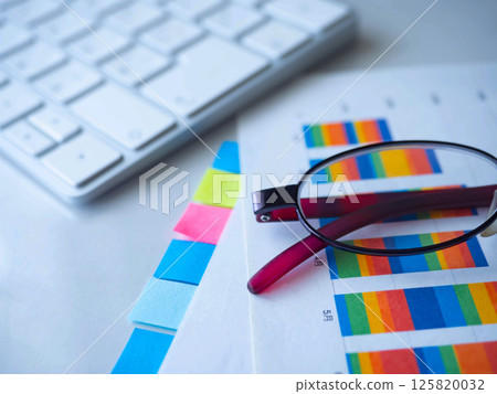 Graphs, documents, keyboard and glasses on a table Graphs, documents, keyboard and glasses on a table 125820032