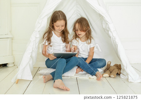 Playful little girl sisters with tablet pc computer in kids tent at home.  125821875