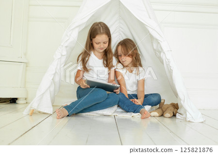 Cheerful child sisters using tablet computer sitting on floor at home Cheerful child sisters using tablet computer sitting on floor at home 125821876