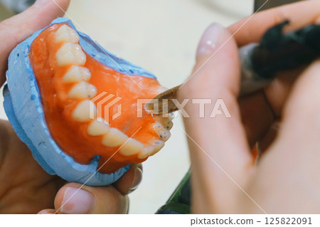 A skilled dental technician meticulously shapes wax into detailed dentures 125822091