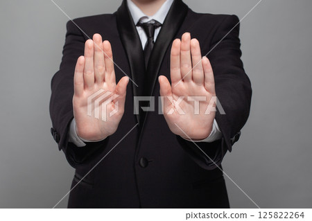 A man in a suit is showing his hands in stop sign. 125822264