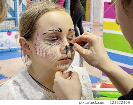 Child girl sitting while makeup artist is making her creative carnival makeup Child girl sitting while makeup artist is making her creative carnival makeup 125822309