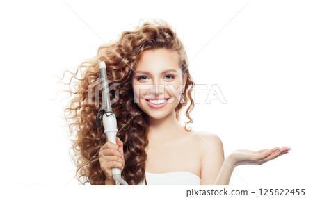Nice woman with healthy long wavy hair  holding empty palm hand and using curlyng iron 125822455