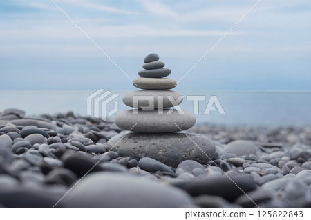 Zen stone pyramid on smooth pebble beach by the sea under soft blue sky, symbolizing peace, stability, mindfulness, and nature's balance in a tranquil and minimalistic coastal environment 125822843