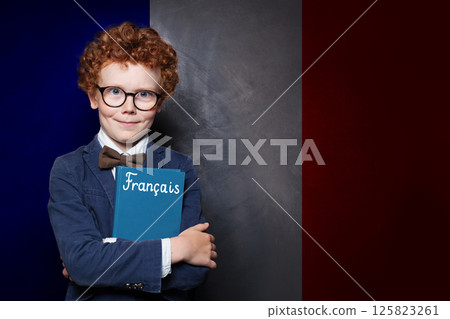 Handsome child boy holding book with the inscription Francais in France standing against French flag 125823261