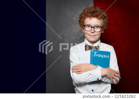 Young school boy holding book with the inscription Francais in France standing against French flag 125823262