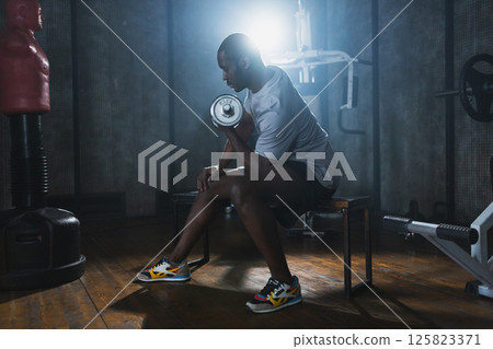 Fitness workout in gym. African American man bodybuilder picking up dumbbells in gym. Workout weight training biceps muscles with dumbbell in fitness club. Man doing sports exercise. Healthy lifestyle 125823371