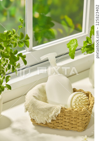 Unlabeled shampoo bottle placed in a wicker basket with a white hand-held comb, lined with a beige burlap cloth. The basket sits on a windowsill surrounded by potted plants. Spa accessories Unlabeled shampoo bottle placed in a wicker basket with a white hand-held comb, lined with a beige burlap cloth. The basket sits on a windowsill surrounded by potted plants. Spa accessories 125823402