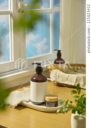 Unbranded amber pump bottle and amber jar placed on an oval marble tray. Behind it is a rattan basket containing burlap, a wooden comb and a cosmetic bottle, displayed on a light brown table. Unbranded amber pump bottle and amber jar placed on an oval marble tray. Behind it is a rattan basket containing burlap, a wooden comb and a cosmetic bottle, displayed on a light brown table. 125823412