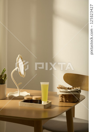 Composition of objects such as essence tubes, amber bottles, flower-shaped table mirrors, cactus pots, displayed on a light brown wooden table. Wooden combs placed in rectangular rattan baskets. Composition of objects such as essence tubes, amber bottles, flower-shaped table mirrors, cactus pots, displayed on a light brown wooden table. Wooden combs placed in rectangular rattan baskets. 125823427