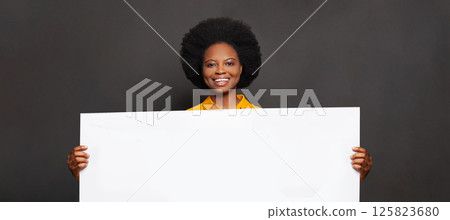 Smiling woman with white empty paper banner in her hand on black background Smiling woman with white empty paper banner in her hand on black background 125823680