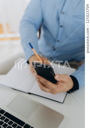 Close up, business man using mobile smart phone and and makes notes in a notebook. makes an appointment, conducts a consultation, social network Close up, business man using mobile smart phone and and makes notes in a notebook. makes an appointment, conducts a consultation, social network 125823704
