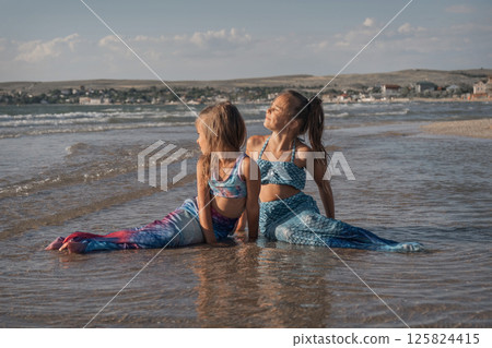 A girl in a mermaid costume on the beach. Sunset on the shore of the blue sea. Childhood happiness, beach, vacation, sunscreen, warm weather, travel. High quality photo A girl in a mermaid costume on the beach. Sunset on the shore of the blue sea. Childhood happiness, beach, vacation, sunscreen, warm weather, travel. High quality photo 125824415