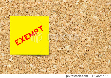 Yellow note paper with word exempt on cork board background with copy space 125824466