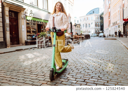 Happy woman rides an electric scooter in the city street on a sunny day. Ecological transport. 125824540